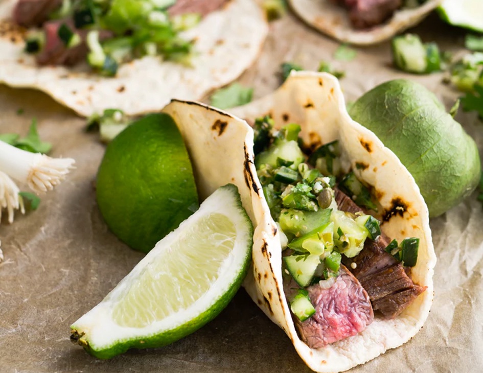 Beef taco with diced greens surrounded by lime wedges